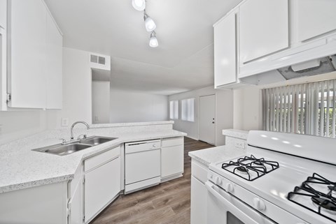 A white kitchen with a stove, sink, and cabinets.