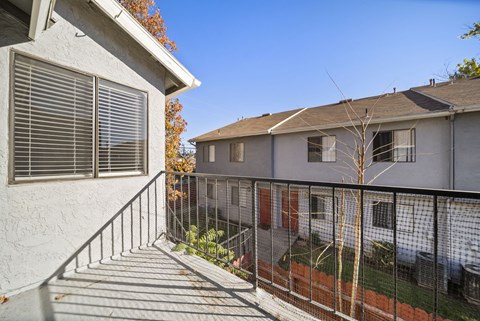 A balcony with a metal railing and a tree in the background.