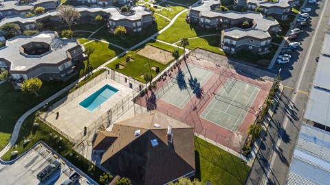 A tennis court is surrounded by a fence and a swimming pool.
