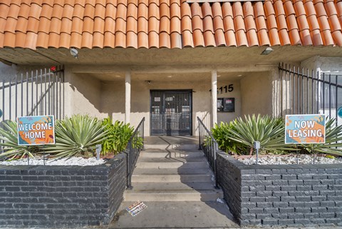 A building with a red tile roof has a sign that says "Welcome Home" and "Now Leasing.".