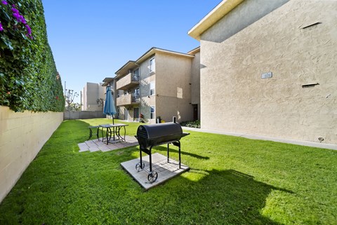A black grill is on a stand in a grassy yard.