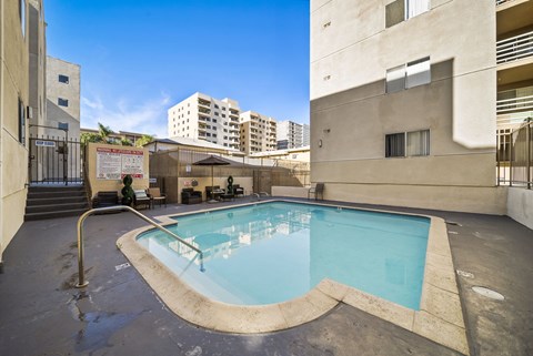 A small pool with a diving board is surrounded by buildings.