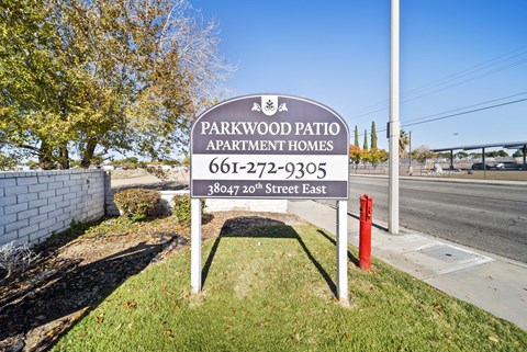 A sign for Parkwood Patio Apartment Homes stands in front of a tree.