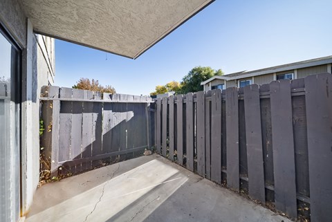 A concrete patio with a grey fence and a white wall.