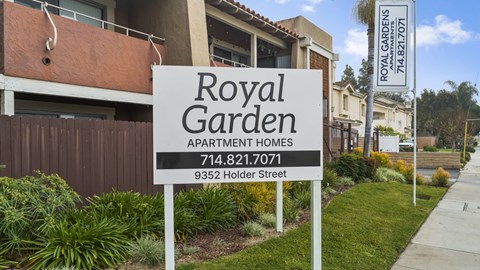 A sign for Royal Garden Apartment Homes stands in front of a building.