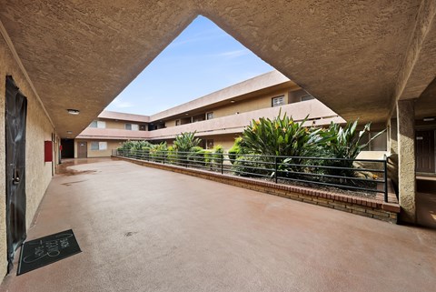 A courtyard with a triangular roof and a fence with plants on it.