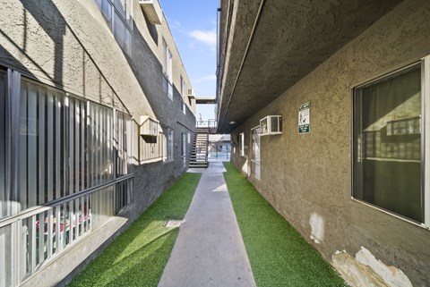 A long, narrow walkway between two buildings with grass on the ground.