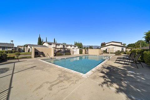A swimming pool surrounded by a concrete patio and lounge chairs.