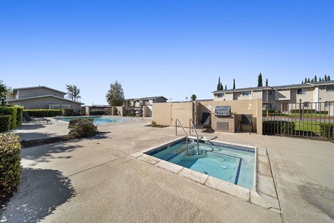 A large outdoor swimming pool surrounded by a concrete patio and buildings.