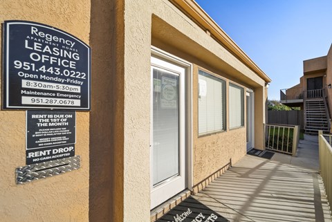A leasing office sign is posted on a wall outside a building.