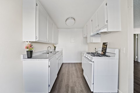 A white kitchen with a sink, stove, and cabinets.