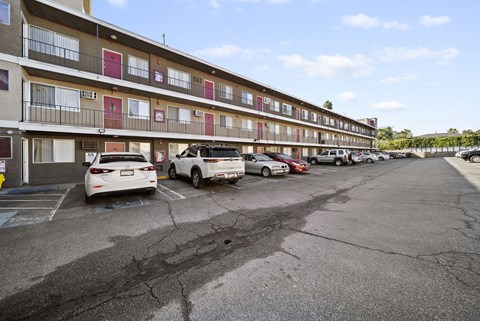 A parking lot in front of a multi-story apartment building with cars parked.