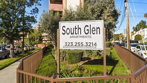 A sign for South Glen Apartments is displayed in front of a fence.