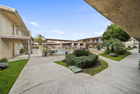 A concrete walkway leads to a pool surrounded by apartment buildings.