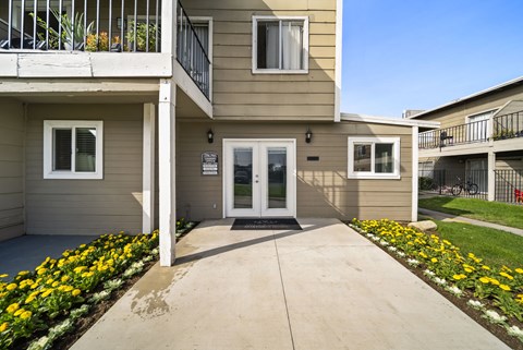 A building with a white door and windows with flower beds in front.