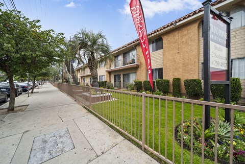 A red banner with white text hangs on a black pole in front of a building.