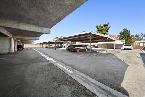 A parking lot with a red car parked in the shade.