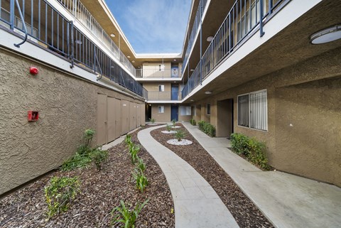 A concrete pathway leads through a landscaped courtyard between two apartment buildings.