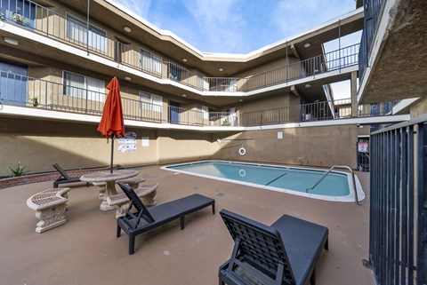 A pool area with a red umbrella and black lounge chairs.