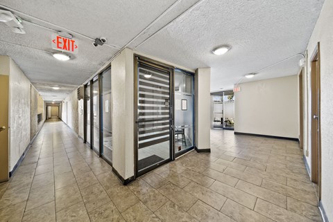 A long hallway with a red exit sign on the ceiling.
