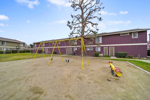 A playground with a yellow swing set and a red slide in front of a red building.