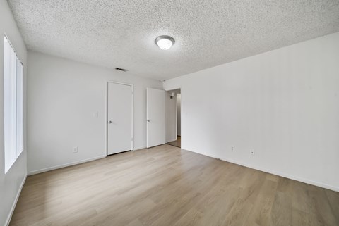 A room with white walls and wooden flooring with a window on the left side.