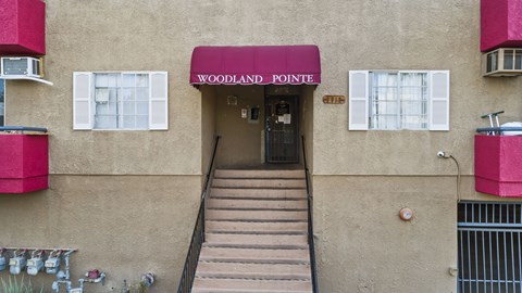 The entrance to a building with a red awning that says Woodland Pointe.