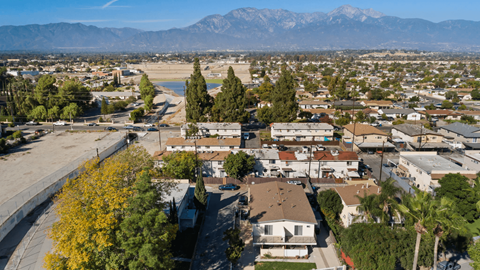 A residential area with houses and trees in the foreground and mountains in the background.