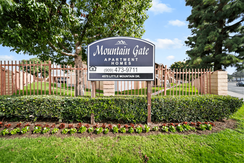 A sign for Mountain Gate Apartment Homes is displayed in front of a fence.