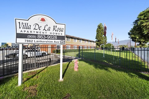 A sign for Villa De La Rosa Apartment Homes stands in front of a building.