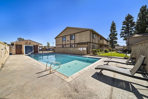 A pool with a slide and sun loungers in front of a building.