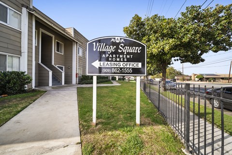 A sign for Village Square Apartments is in front of a building.