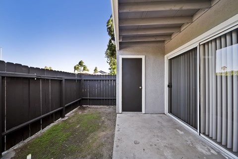 A black door is on the right side of a concrete patio.