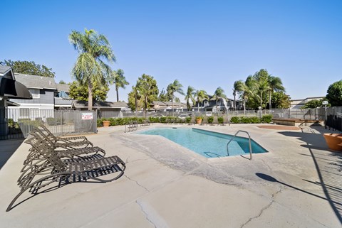 A pool with chairs around it and a fence in the background.