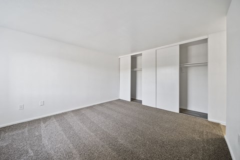 A room with grey carpet and white walls with a row of cupboards.
