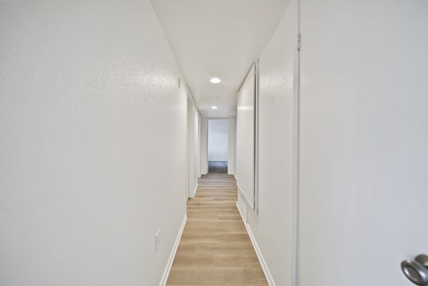 A long hallway with white walls and wood flooring.