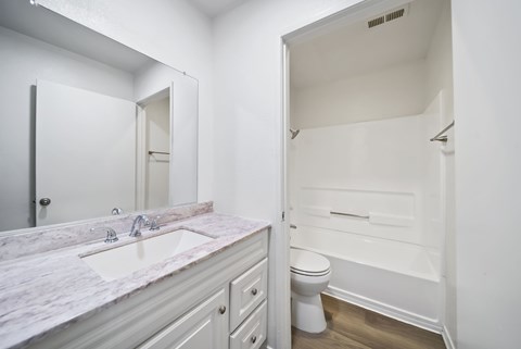 A white bathroom with a marble counter top and a toilet.
