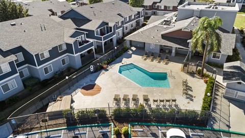 A large swimming pool surrounded by a fence and chairs is in the center of a residential area.