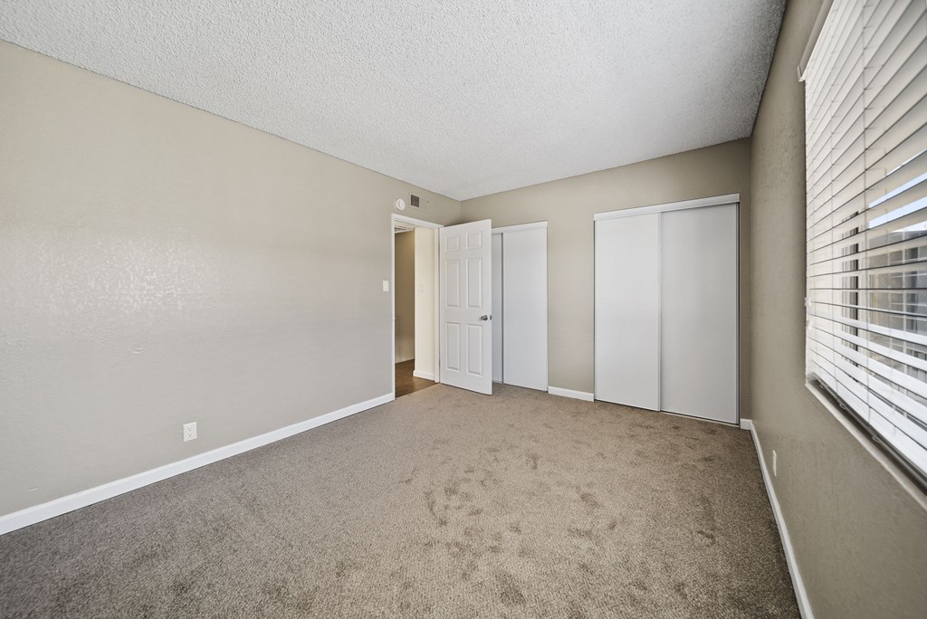 A room with a carpeted floor and a window with blinds.