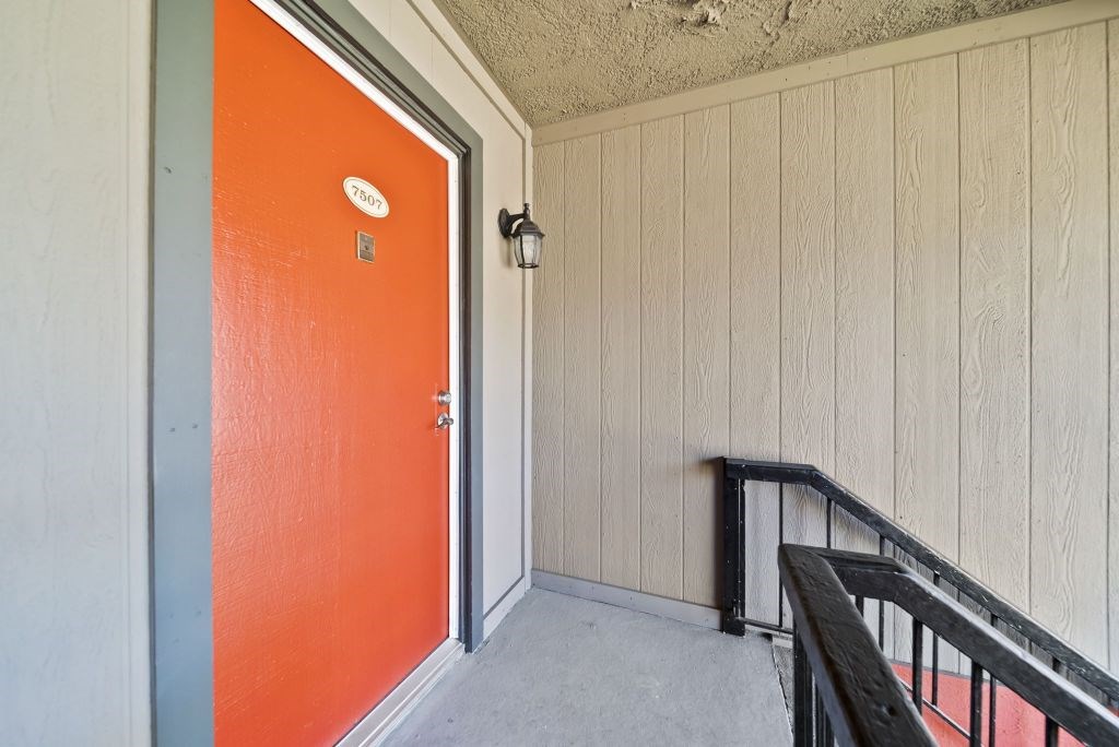 A bright orange door with a silver handle and a small round plate above it.