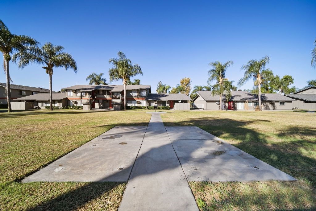 A concrete pathway leads to a row of houses with palm trees in the background.