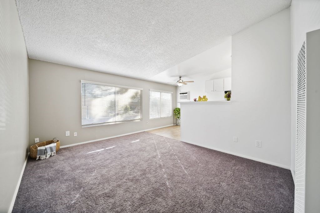 A sparsely furnished room with a carpeted floor and a window with blinds.