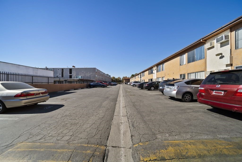 A parking lot with cars parked on both sides and apartment buildings in the background.