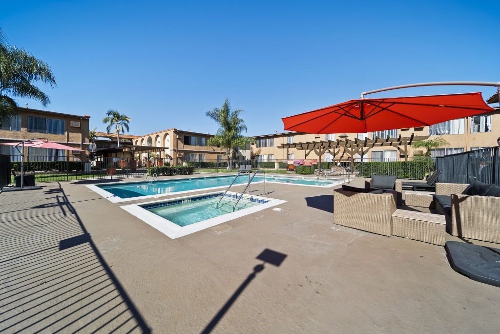 A pool with a red umbrella and a building in the background.