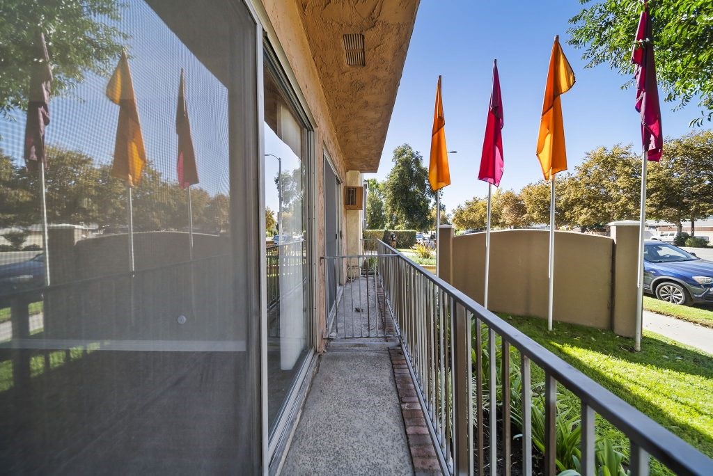 A balcony with a metal railing and a glass door leading to a patio with orange flags.