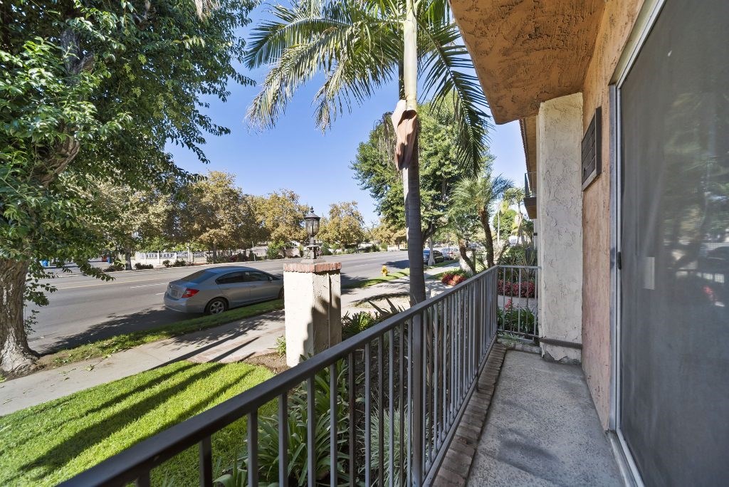 A balcony with a metal railing and a view of a street with a car and trees.