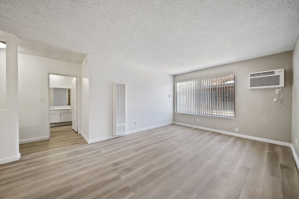 A spacious room with wooden flooring and a window with blinds.