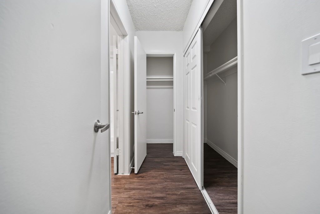 A white hallway with a door on the left and a refrigerator on the right.