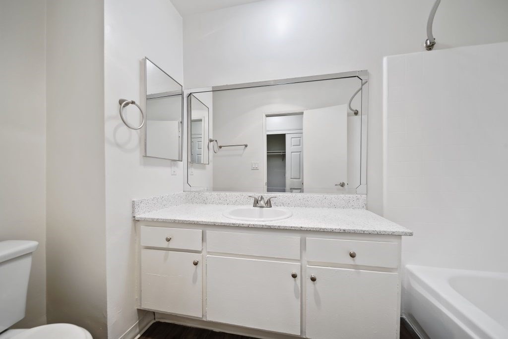 A white bathroom with a sink, mirror, and bathtub.
