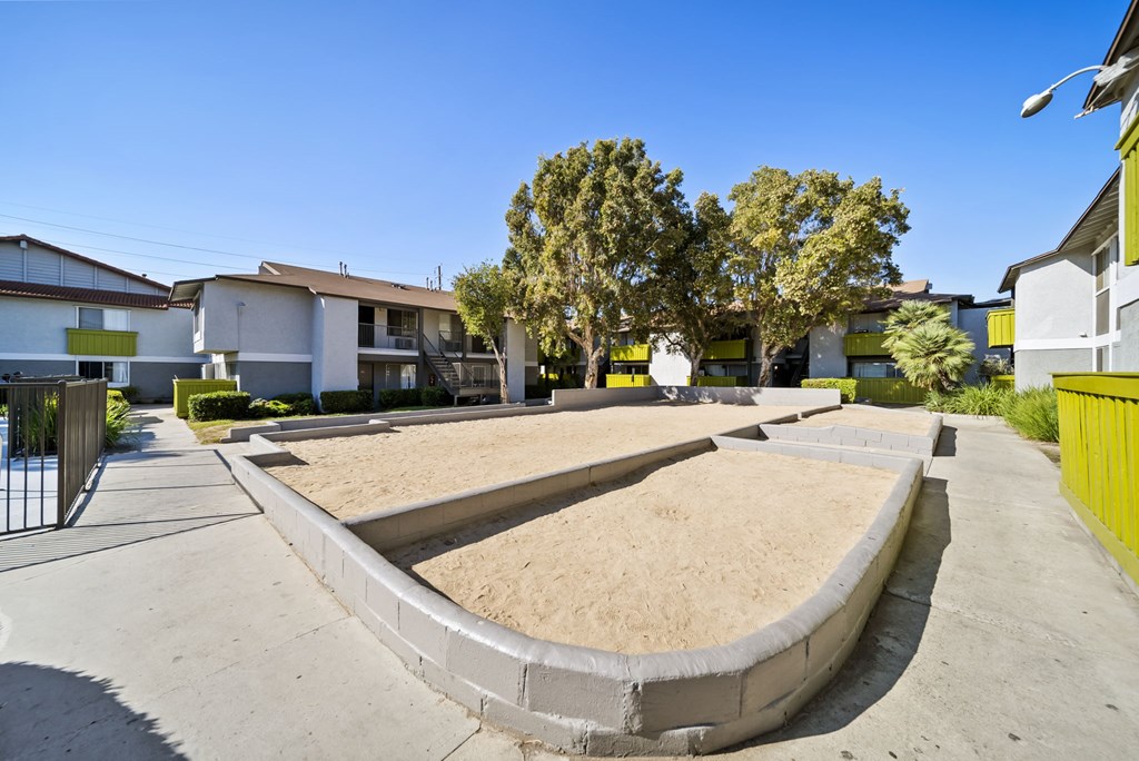 A sand pit in the middle of a concrete area with houses in the background.